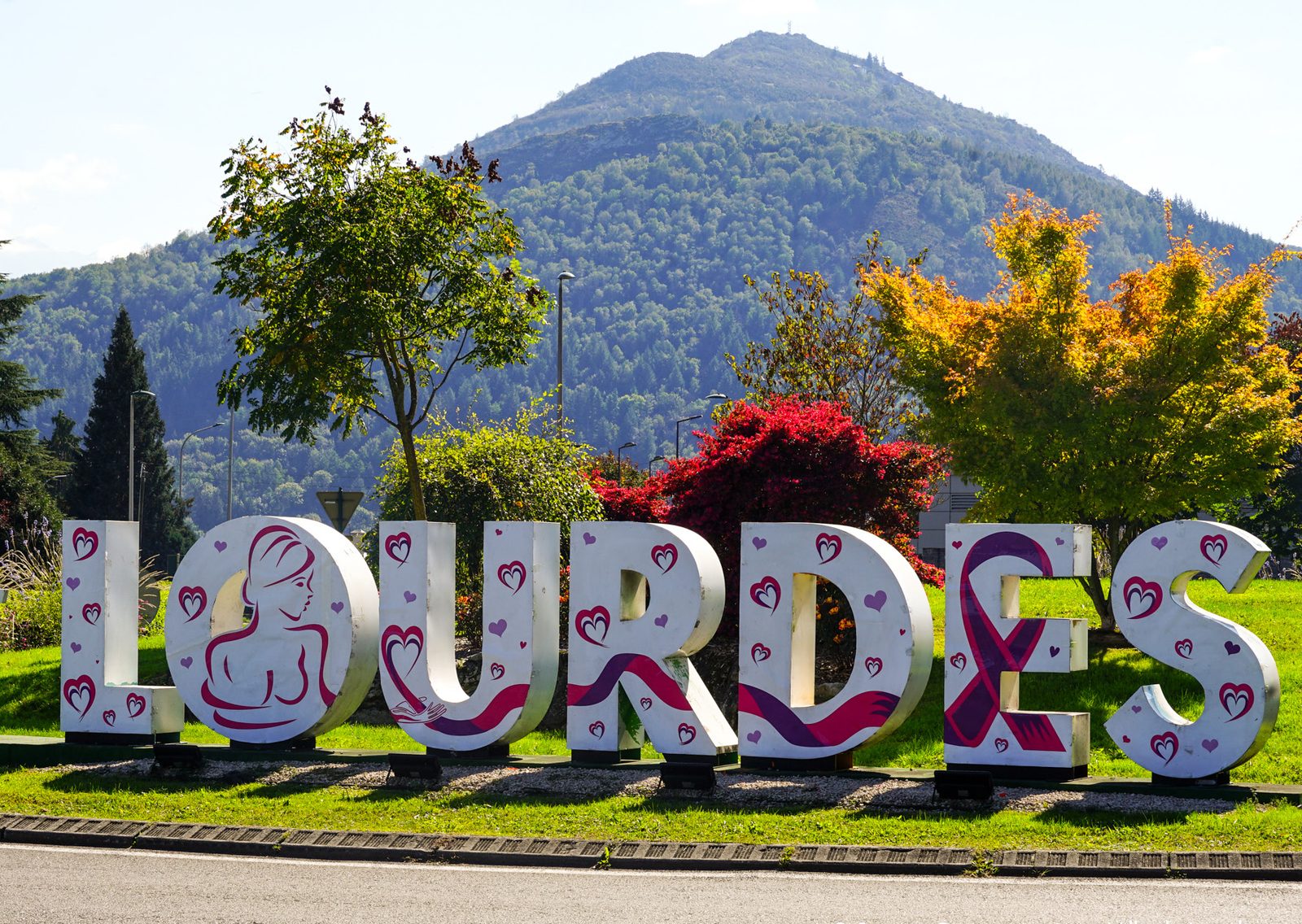 Les grandes lettres LOURDES décorées aux couleurs d'Octobre Rose, avec le Pic du Jer en arrière-plan